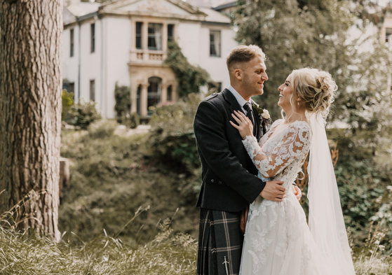 Smiling bride and groom embrace outside Norwood Hall Hotel in Aberdeen